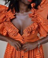 Model wearing The Kemist Barletta Backless Dress in Orange on a plain cream backdrop. 