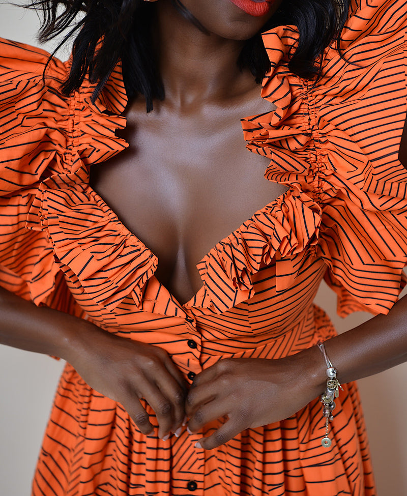 Model wearing The Kemist Barletta Backless Dress in Orange on a plain cream backdrop. 
