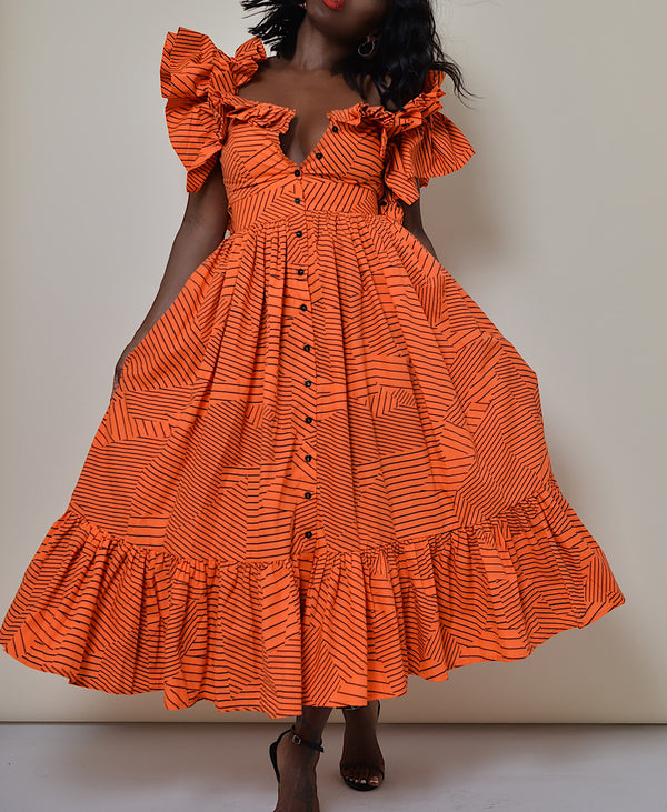 Model wearing The Kemist Barletta Backless Dress in Orange on a plain cream backdrop. 