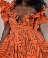 Model wearing The Kemist Barletta Backless Dress in Orange on a plain cream backdrop. 