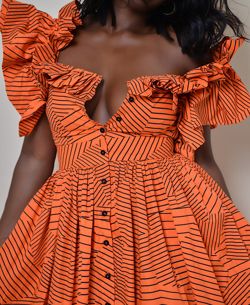 Model wearing The Kemist Barletta Backless Dress in Orange on a plain cream backdrop. 