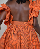 Model wearing The Kemist Barletta Backless Dress in Orange on a plain cream backdrop. 