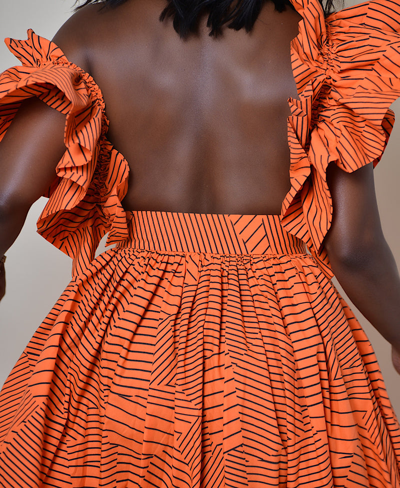 Model wearing The Kemist Barletta Backless Dress in Orange on a plain cream backdrop. 