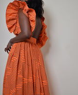 Model wearing The Kemist Barletta Backless Dress in Orange on a plain cream backdrop. 