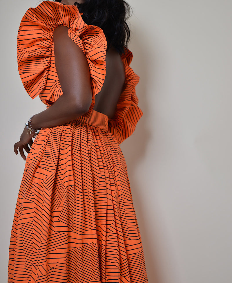 Model wearing The Kemist Barletta Backless Dress in Orange on a plain cream backdrop. 