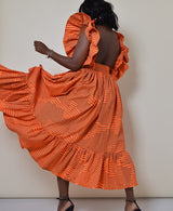 Model wearing The Kemist Barletta Backless Dress in Orange on a plain cream backdrop. 