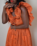 Model wearing The Kemist Barletta Backless Dress in Orange on a plain cream backdrop. 