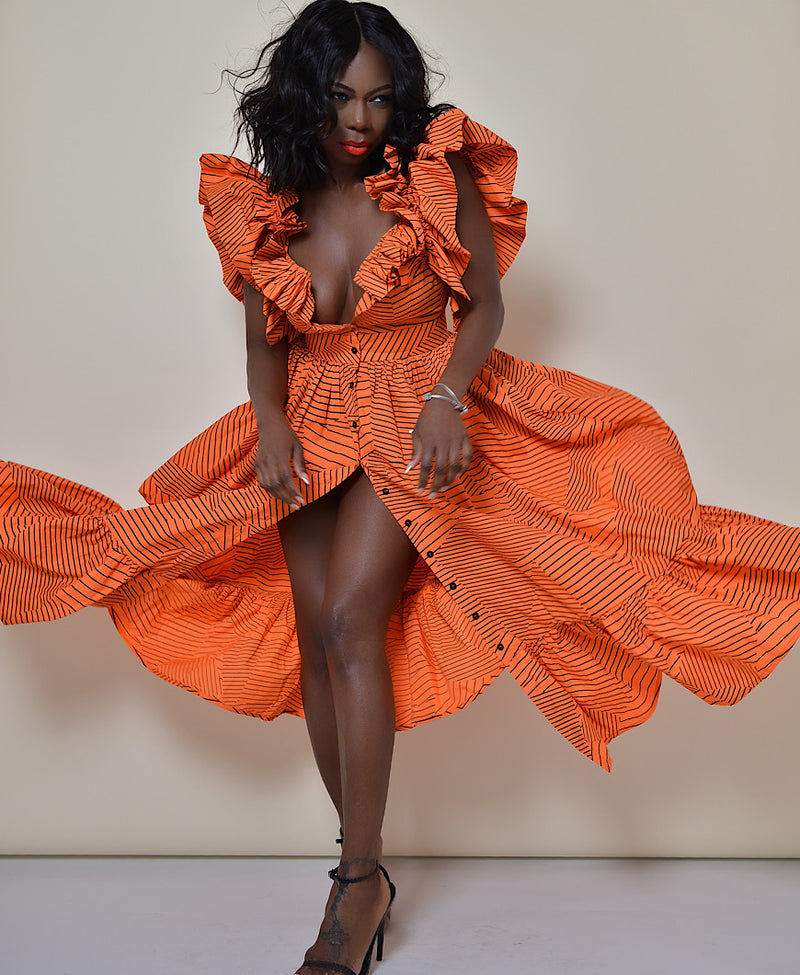 Model wearing The Kemist Barletta Backless Dress in Orange on a plain cream backdrop. 