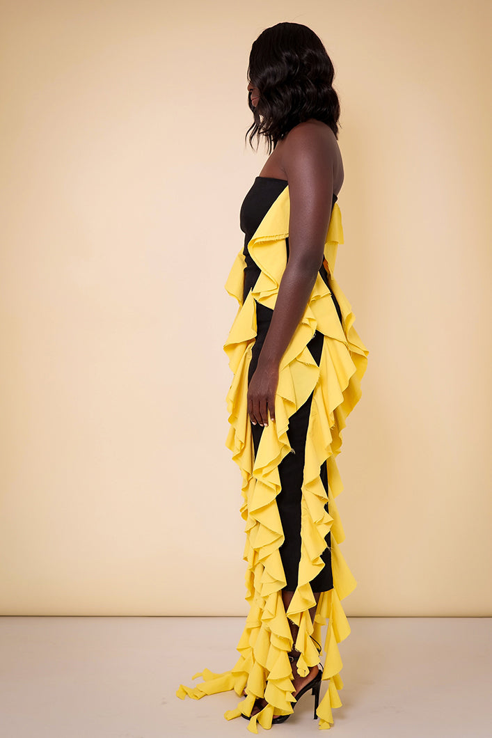 Model wearing The Kemist Seville Strapless Waterfall Ruffle Dress in Black and Yellow on a plain cream backdrop.