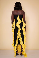 Model wearing The Kemist Seville Strapless Waterfall Ruffle Dress in Black and Yellow on a plain cream backdrop.