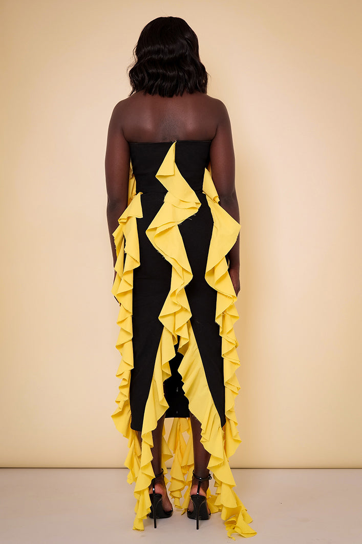 Model wearing The Kemist Seville Strapless Waterfall Ruffle Dress in Black and Yellow on a plain cream backdrop.