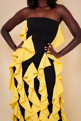 Model wearing The Kemist Seville Strapless Waterfall Ruffle Dress in Black and Yellow on a plain cream backdrop.