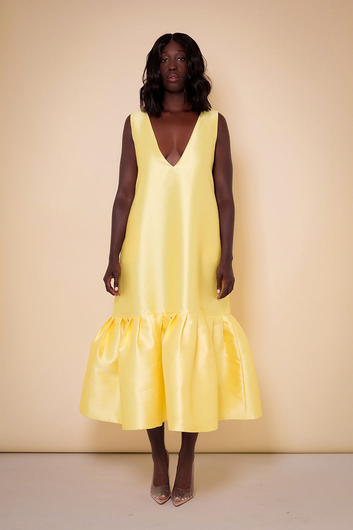 Model wearing The Kemist Syracuse pleated hem oversized dress in yellow on a plain cream backdrop.