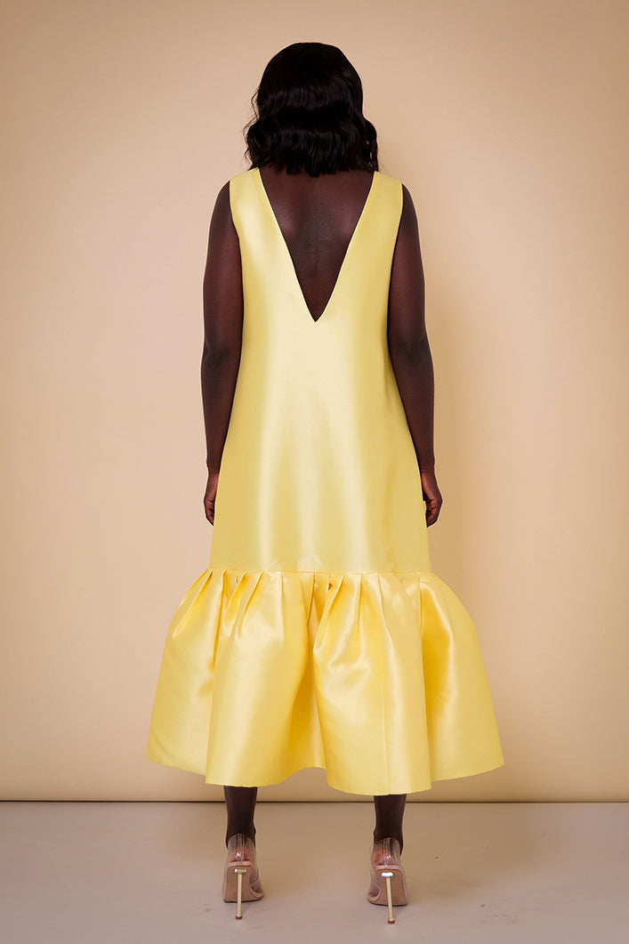 Model wearing The Kemist Syracuse pleated hem oversized dress in yellow on a plain cream backdrop.