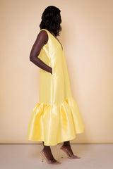 Model wearing The Kemist Syracuse pleated hem oversized dress in yellow on a plain cream backdrop.