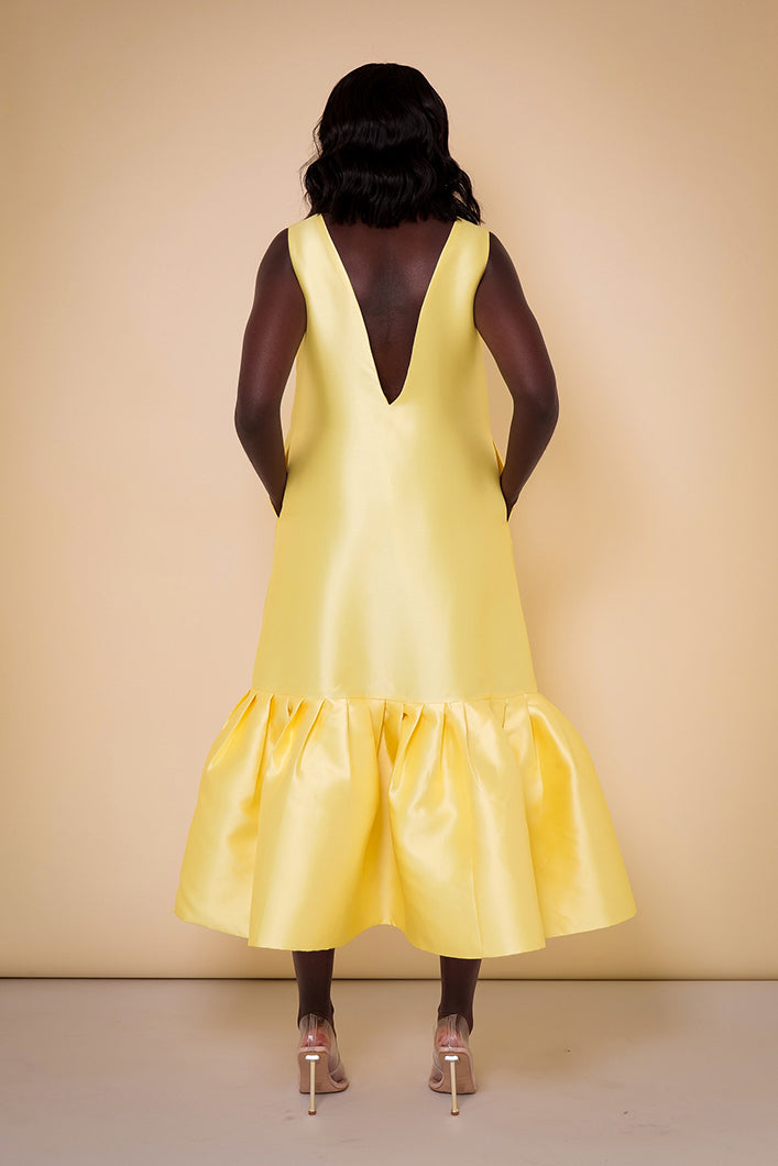 Model wearing The Kemist Syracuse pleated hem oversized dress in yellow on a plain cream backdrop.