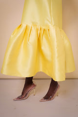 Model wearing The Kemist Syracuse pleated hem oversized dress in yellow on a plain cream backdrop.