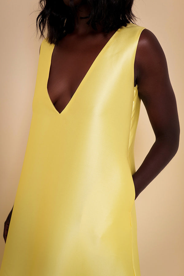 Model wearing The Kemist Syracuse pleated hem oversized dress in yellow on a plain cream backdrop.